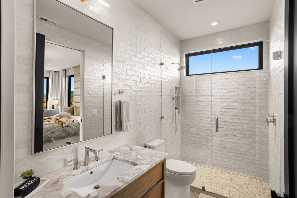 White tiled en-suite bathroom with a walk-in shower, marble vanity and a high window
