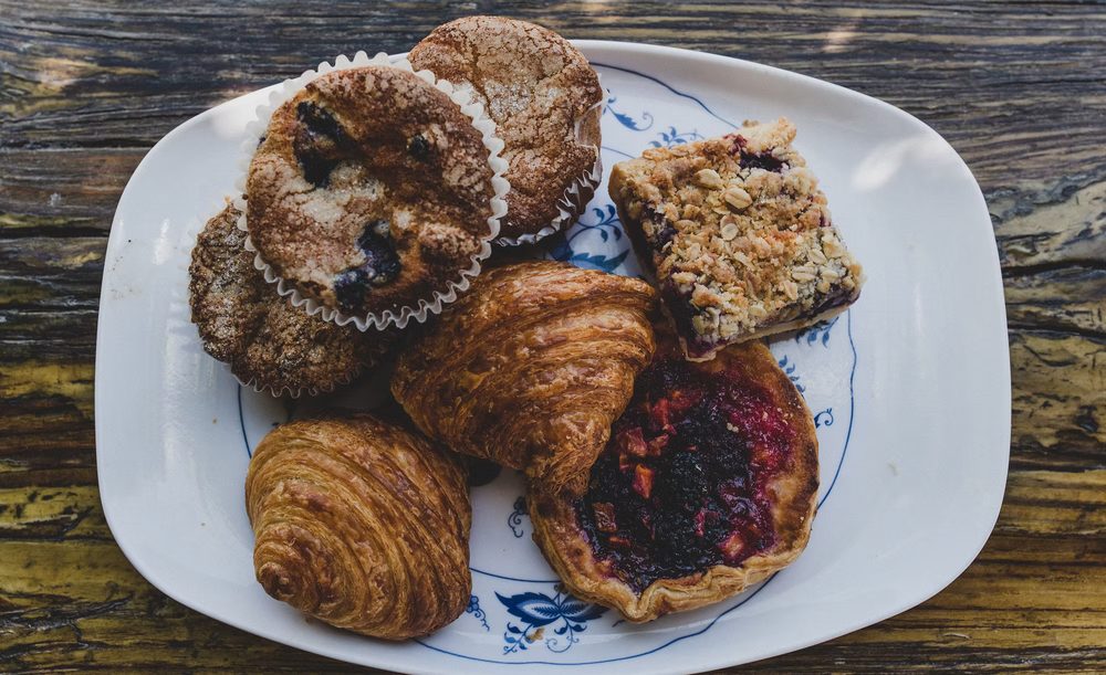Pastries from Wildflour Bakery on a blue-and-white plate: croissants, muffins, a berry crumb bar and a fruit tart